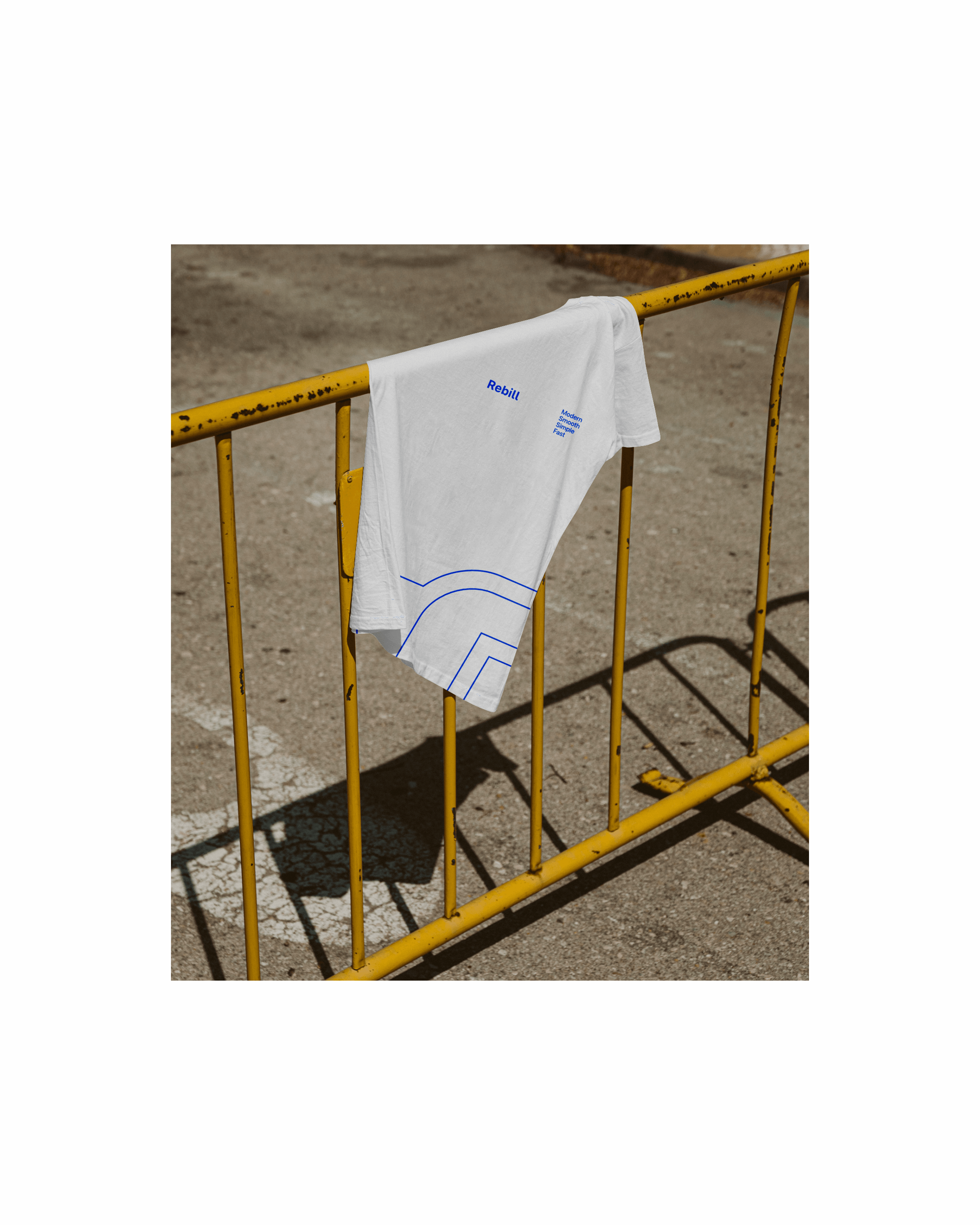 White t-shirt with oversized blue Rebill logo line graphic draped over a yellow street barrier, showcasing Kundo Studio’s confident, minimal visual identity for the LATAM payments infrastructure brand.